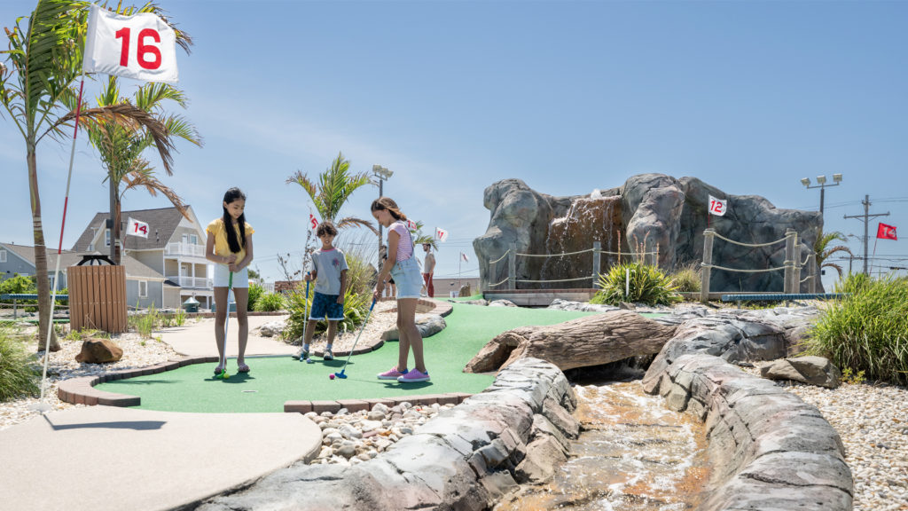 Three kids enjoy a round of miniature golf outside at Lighthouse Point at Jenkinson's Boardwalk