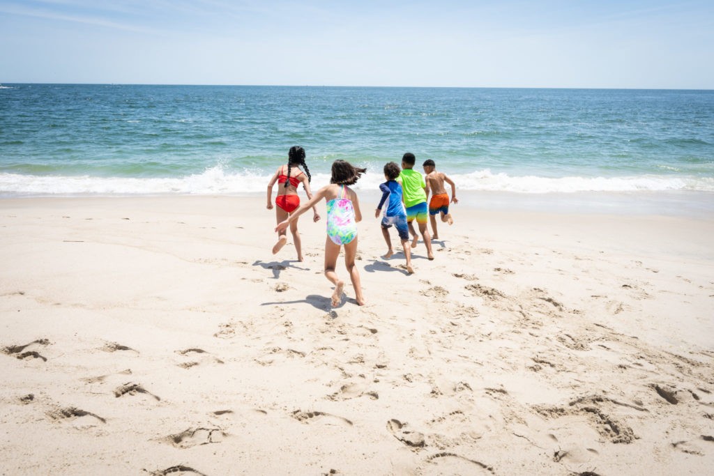 Five kids run toward the ocean in the sand at the beach located at Jenkinson's Boardwalk