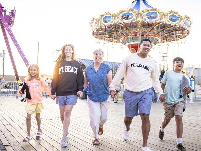 A smiling family walks on Jenkinson’s Boardwalk with rides in the background.