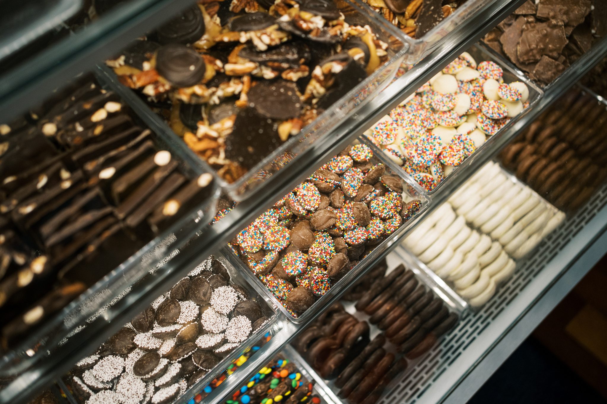 Assortment of gourmet chocolates and candies displayed in clear glass display cases.