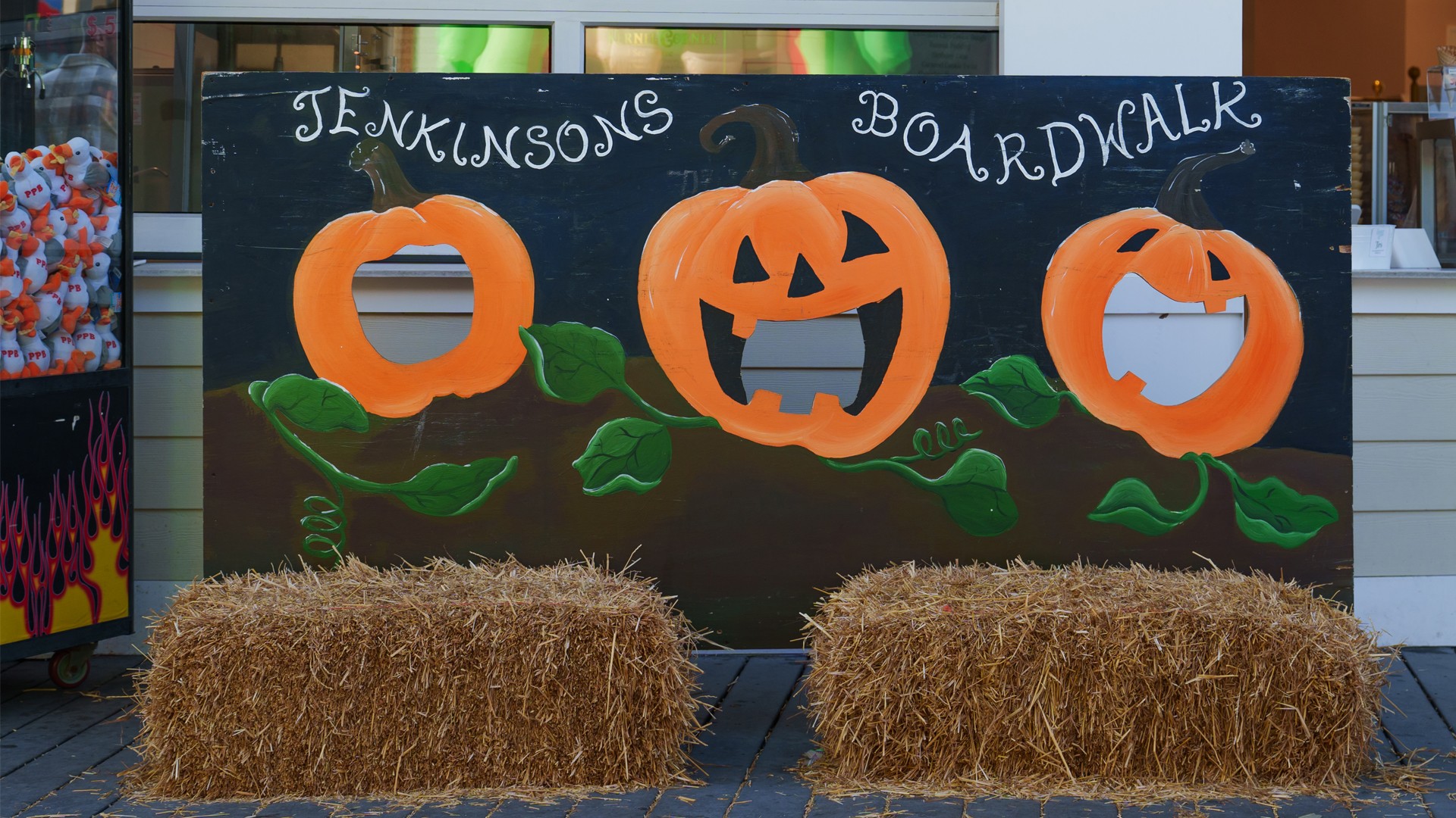 A pumpkin-themed photo board at Jenkinson’s Boardwalk with three cutout faces and hay bales in front.